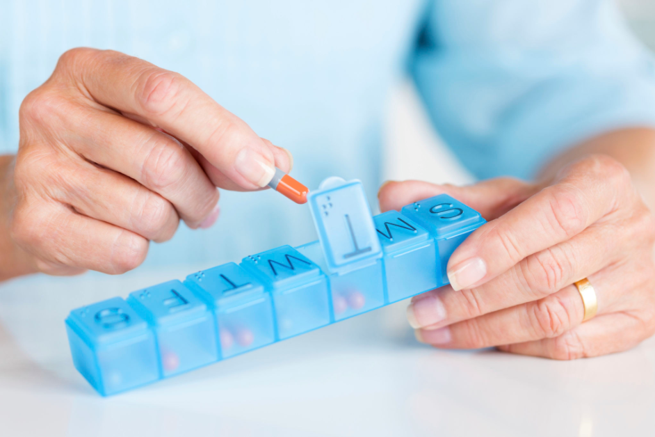 Close-up image of individual taking capsules out of a medication pill box - Courtesy Microsoft Designer